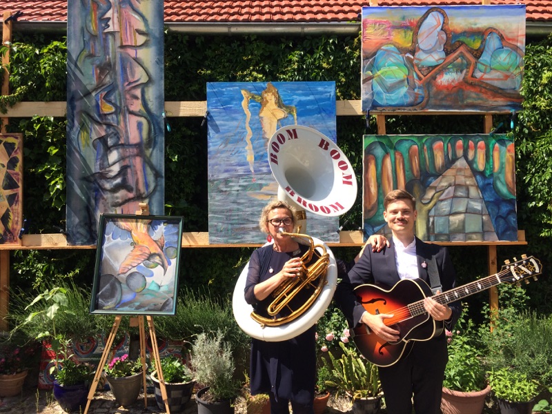 Heike Besen und Julius mit Sousaphon und Gitarre vor bemalten Leinwänden beim Kunstfest in Tiefthal.